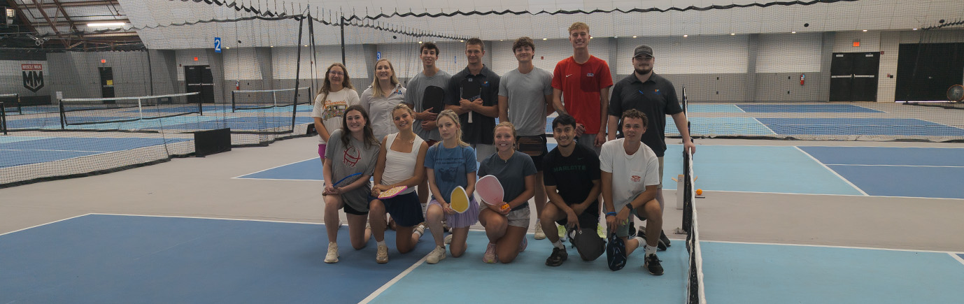 Interns posing in two rows on a pickleball court