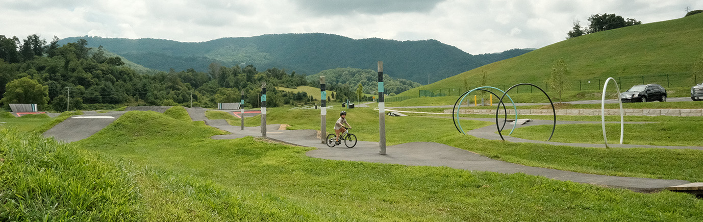 Raccoon creek bike park in Haywood county - showing boy biking between poles on a bicycle pump track with hills and mountains in the background